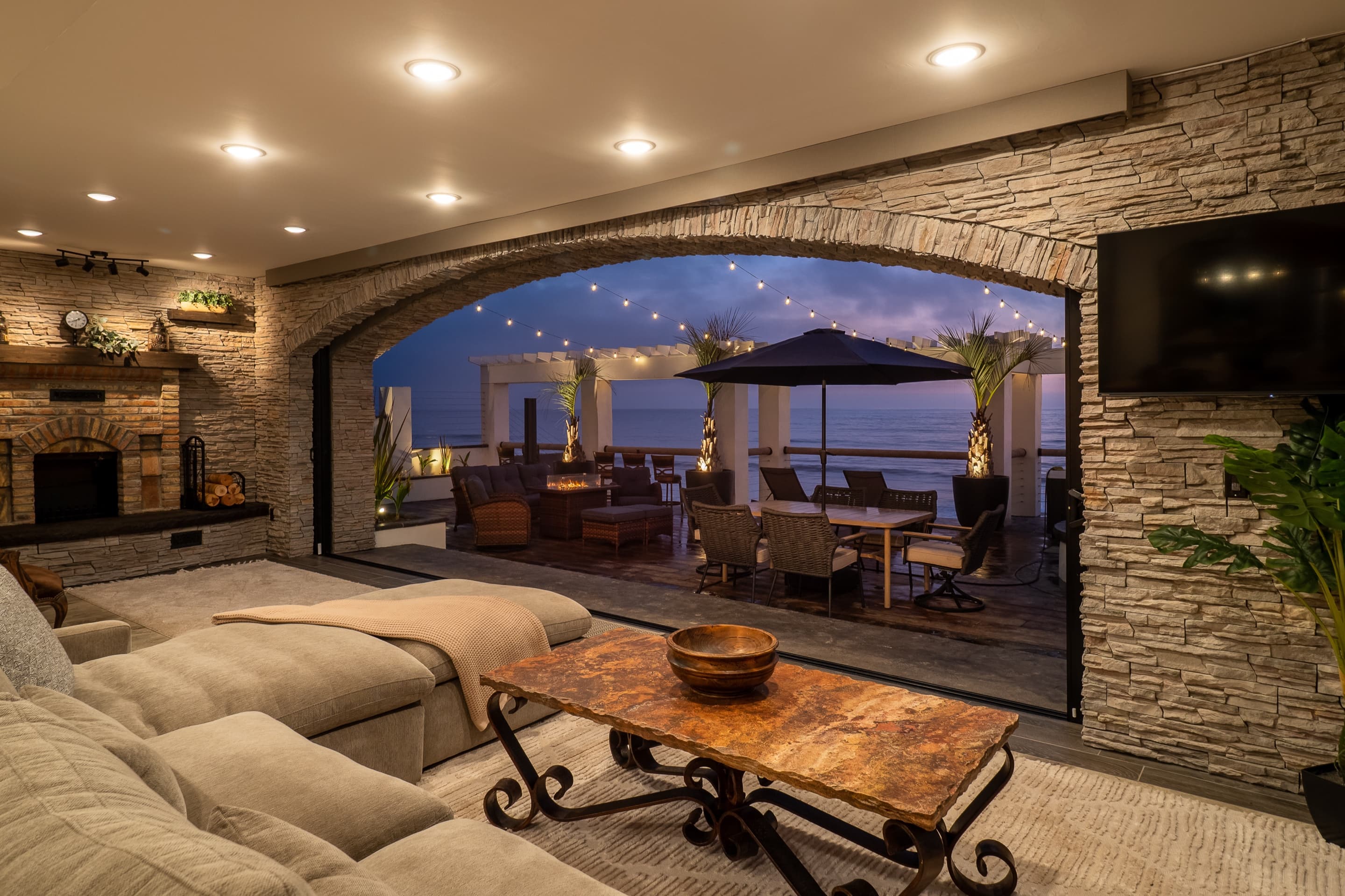 Living room opening through a stone arch onto the ocean-view deck at dusk